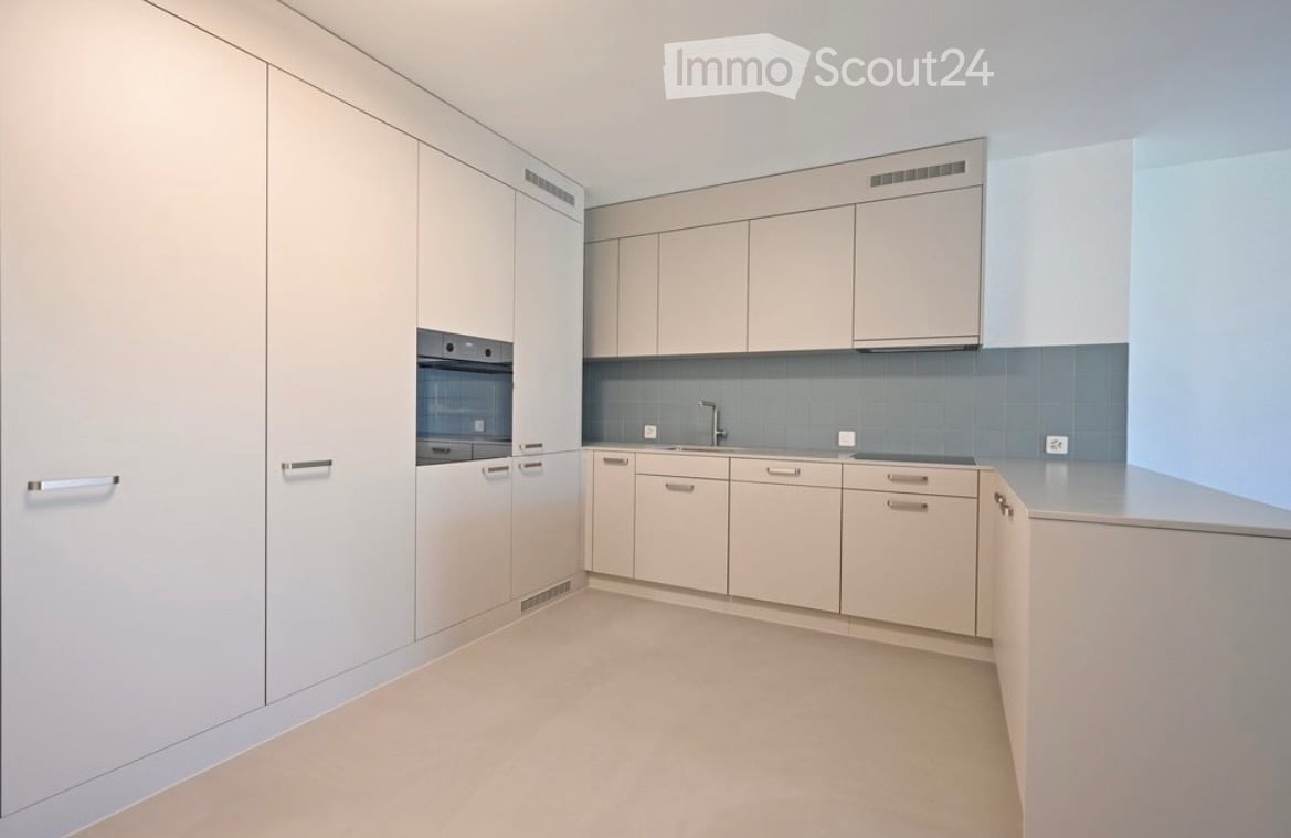 Modern, minimalist kitchen with light-colored cabinets, a central island, and a sink with a faucet.