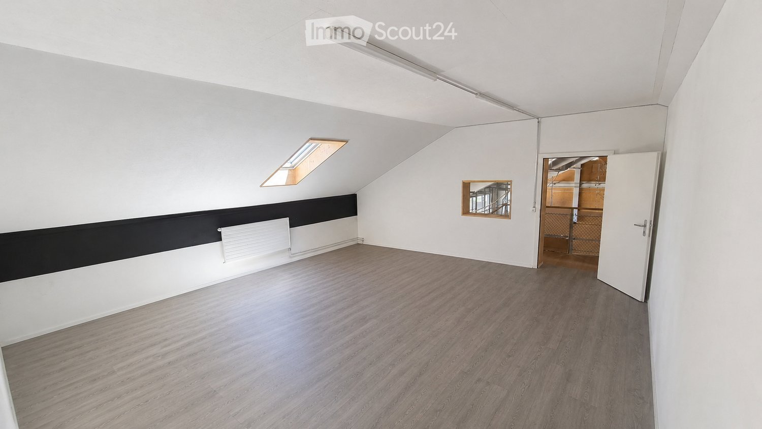 Empty attic room with wooden flooring, white walls, and a skylight window. No furniture or equipment present.