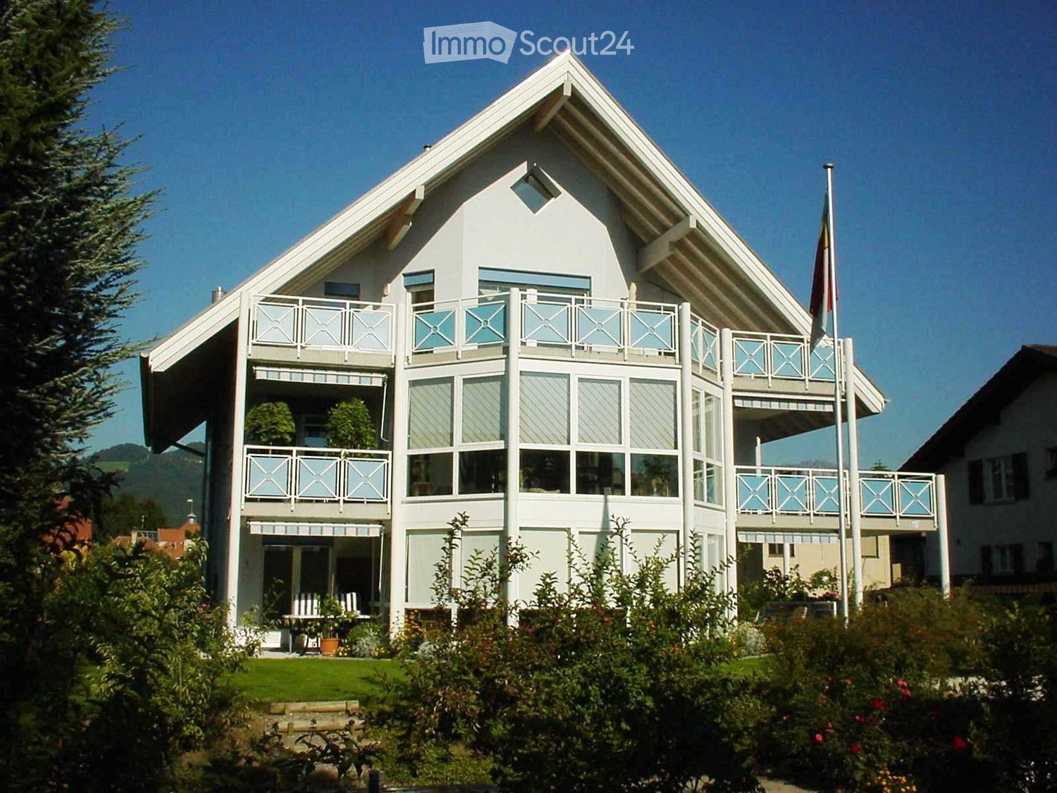 Two-story white house with multiple balconies, large windows, and a well-maintained garden.