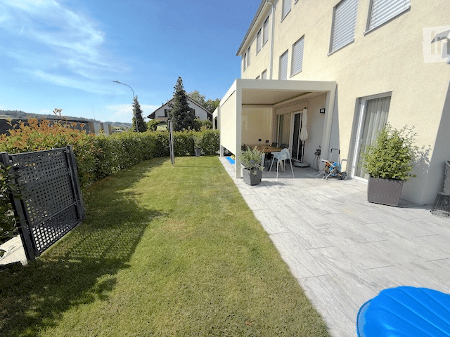 Well-maintained garden with a neatly trimmed lawn, a black metal gate, and a covered patio area with outdoor furniture.