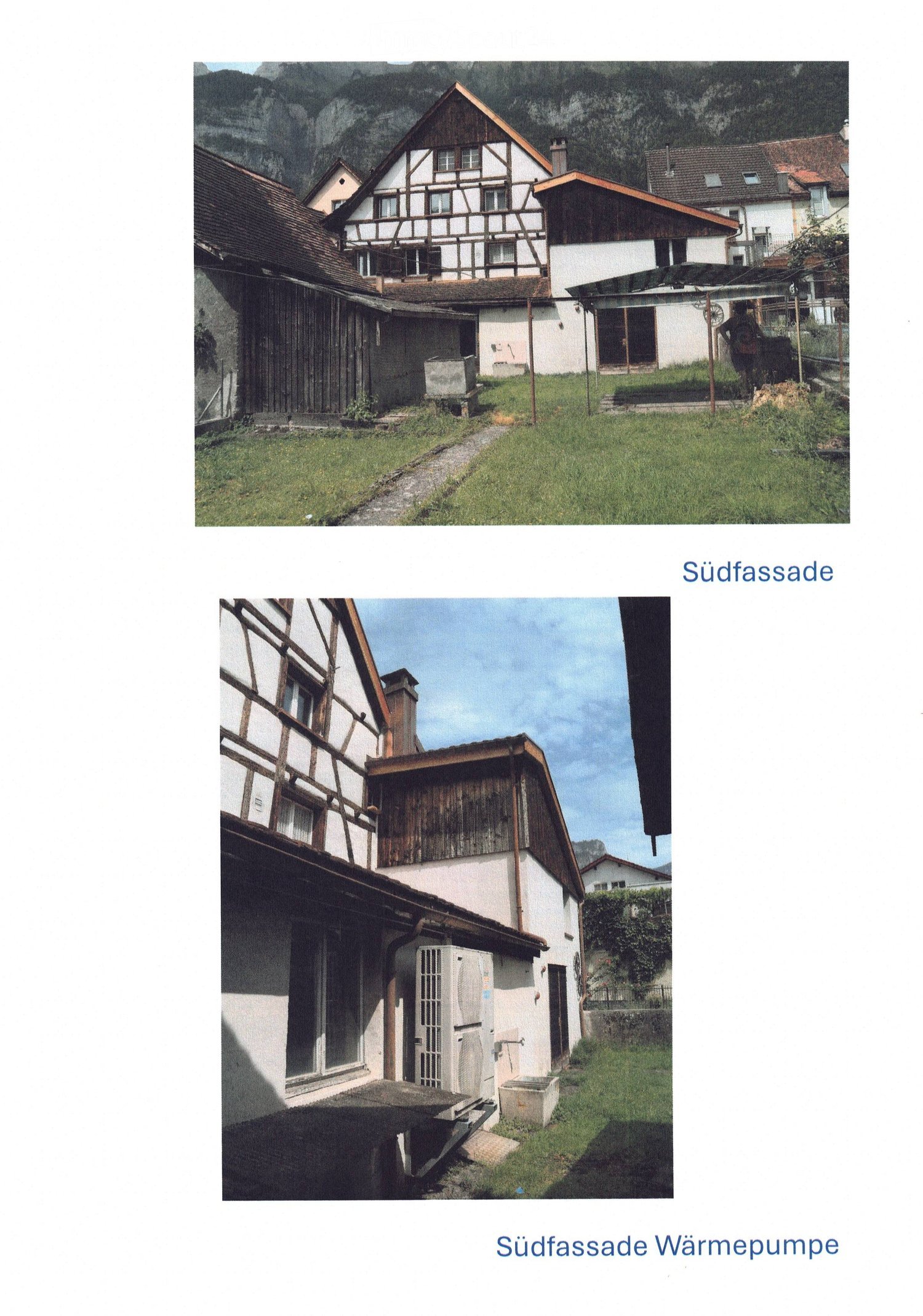 Traditional half-timbered houses with pitched roofs, surrounded by grassy areas and mountains in the background.