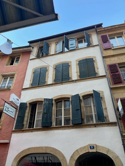 Classic European building with multiple stories, green shutters, arched ground-floor windows, and a visible address number.