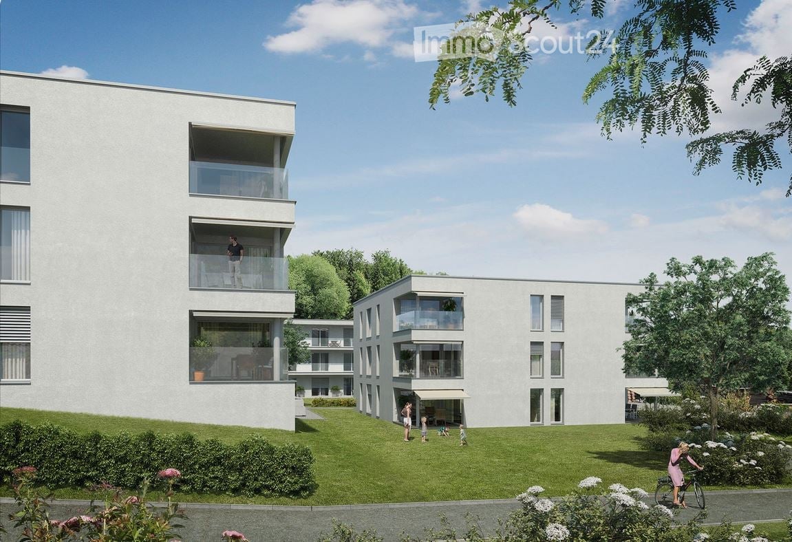 Modern multi-story residential building with balconies, surrounded by a well-maintained lawn and trees.