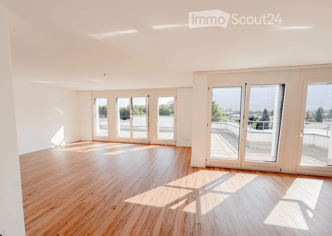 Empty room with wooden flooring, large windows, and sliding doors leading to a balcony with a scenic view.