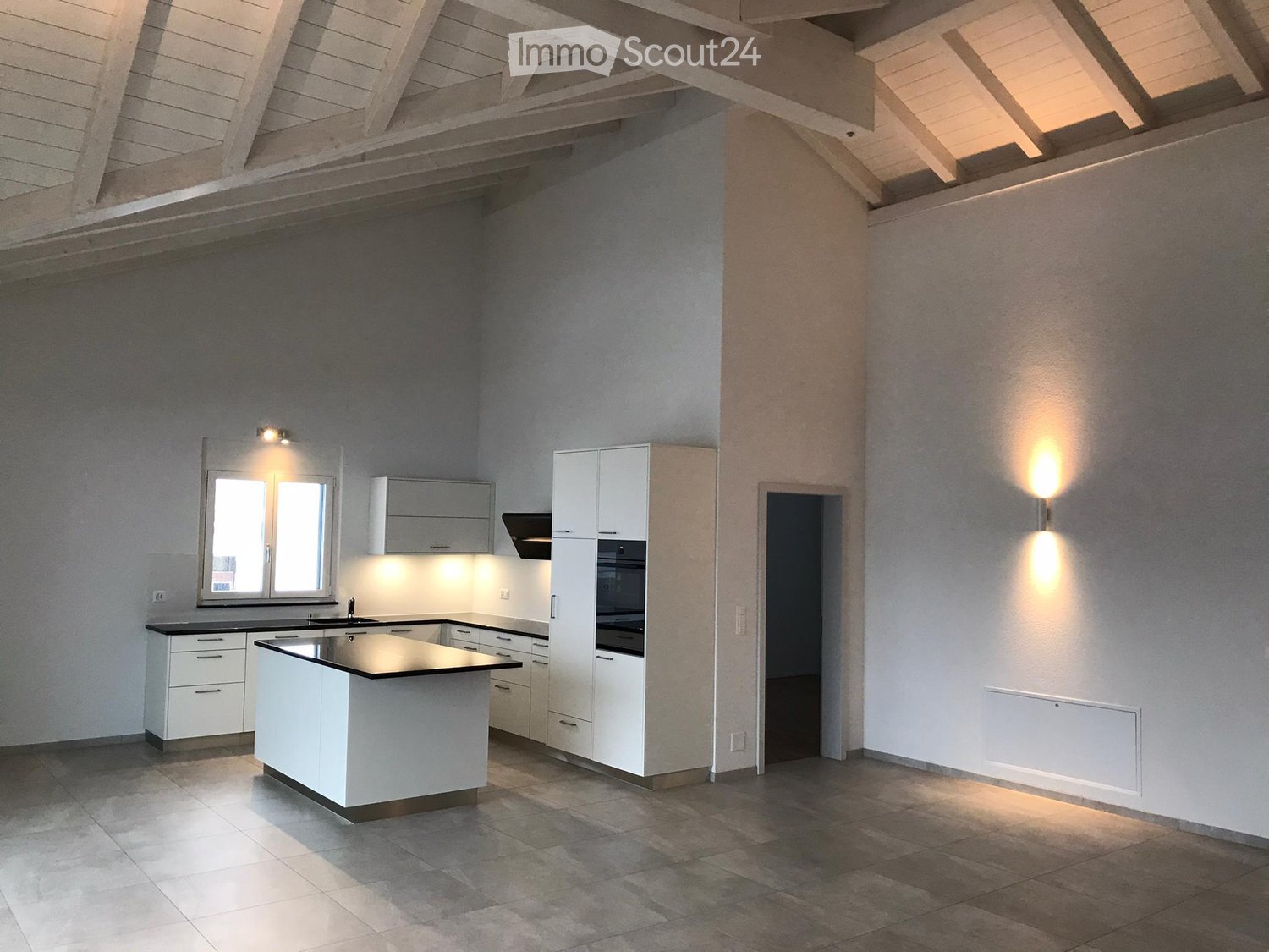 Modern kitchen with white cabinets, a central island, and built-in appliances, featuring large windows and warm lighting.