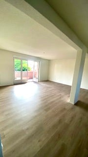 Empty room with light wooden flooring, white walls, and large sliding glass doors leading to an outdoor area.