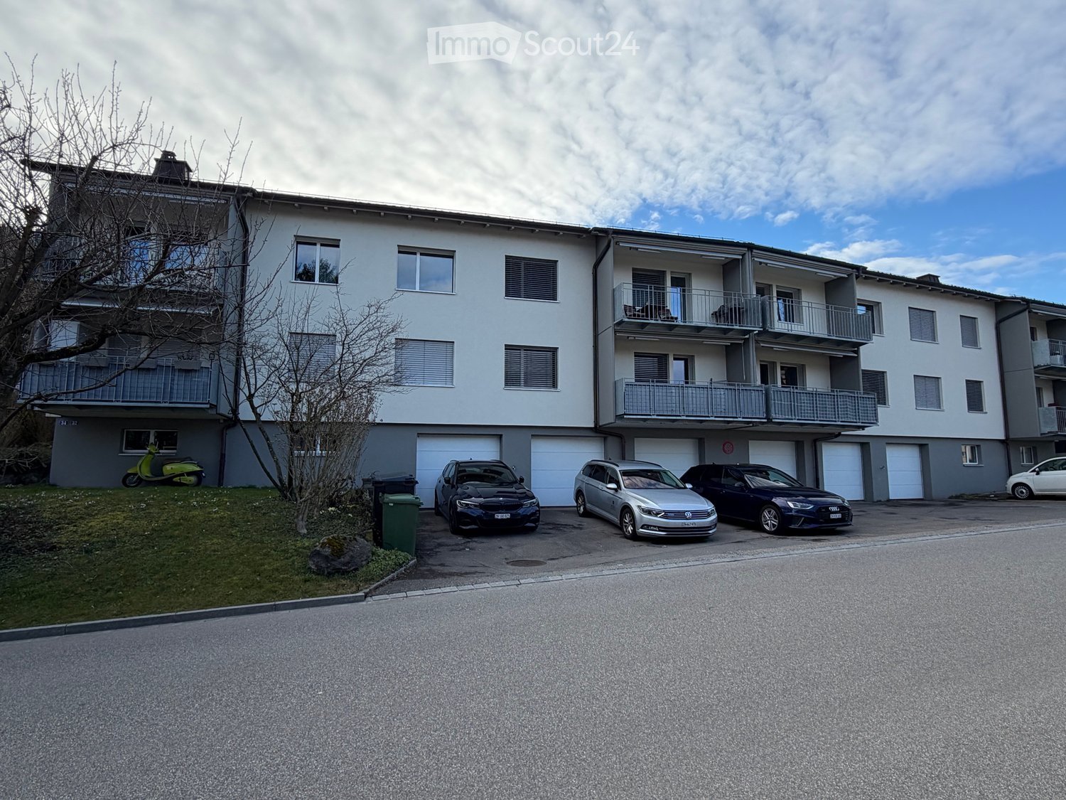 Modern multi-story apartment building with balconies, garage, and several parked cars.