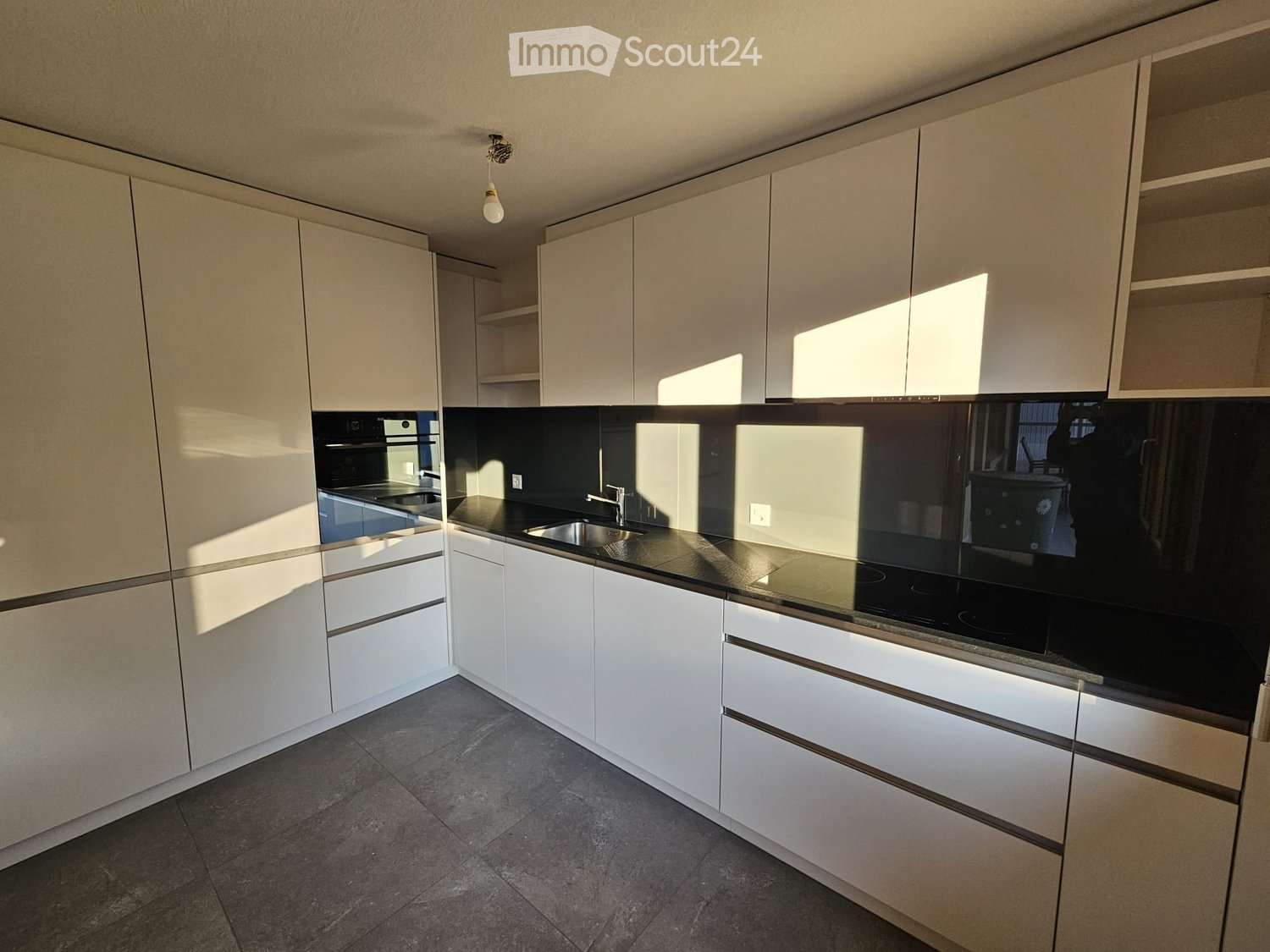 Modern kitchen with white cabinets, black countertops, and stainless steel appliances, including a sink and oven.