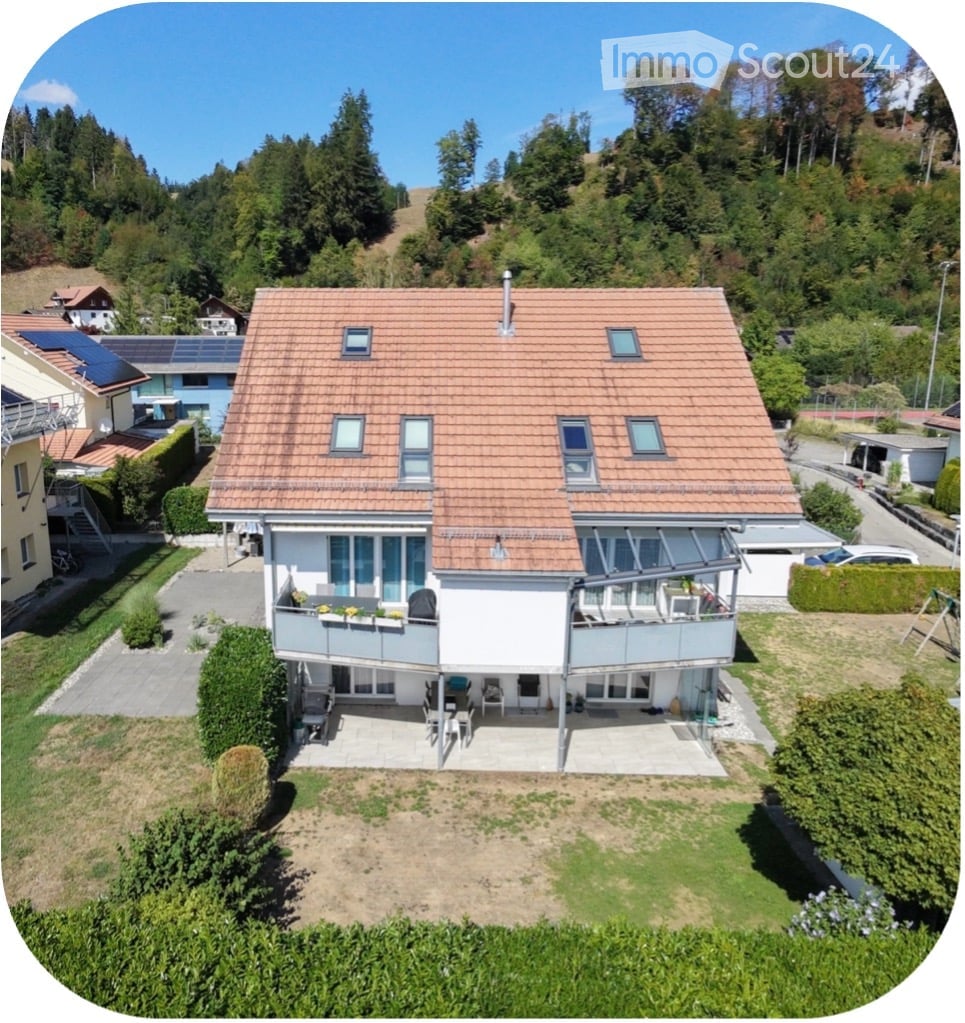 A two-story house with a red-tiled roof, multiple windows, and a balcony area with outdoor furniture.
