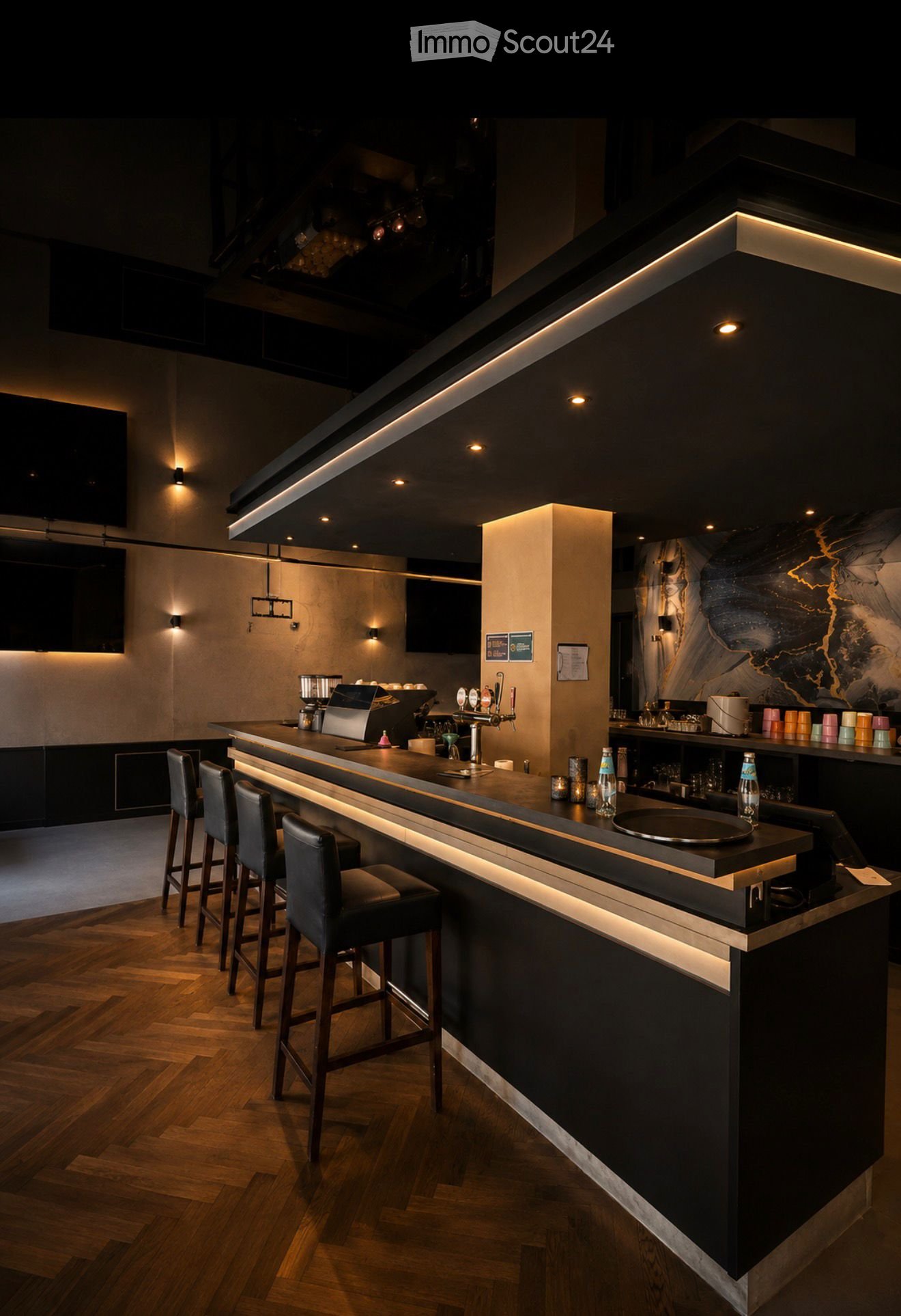Modern bar area with a sleek black and white counter, bar stools, coffee machine, beer tap, and various bottles and cups on the counter.