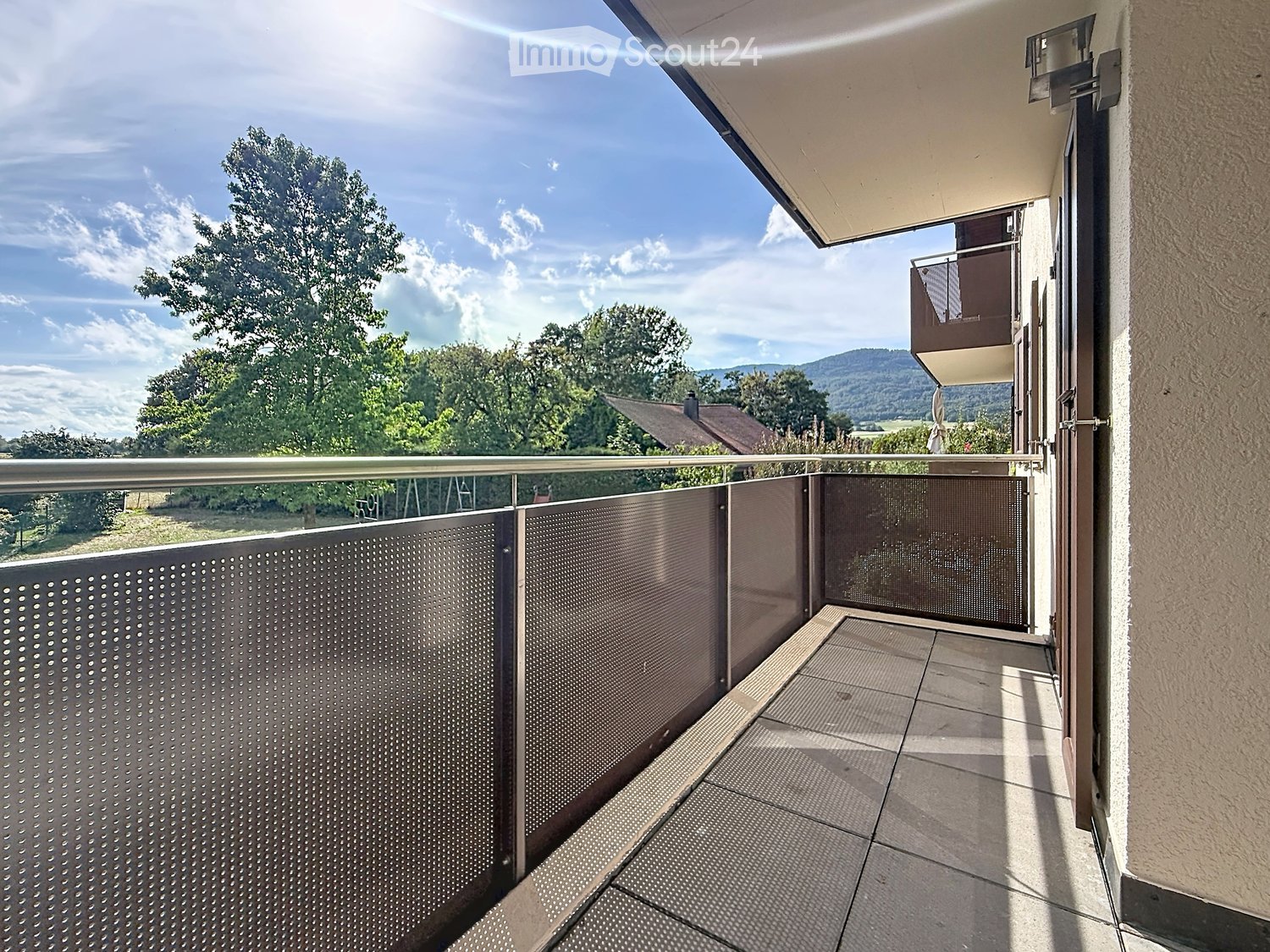 Balcony with metal railing, tiled floor, and scenic view of trees and hills.