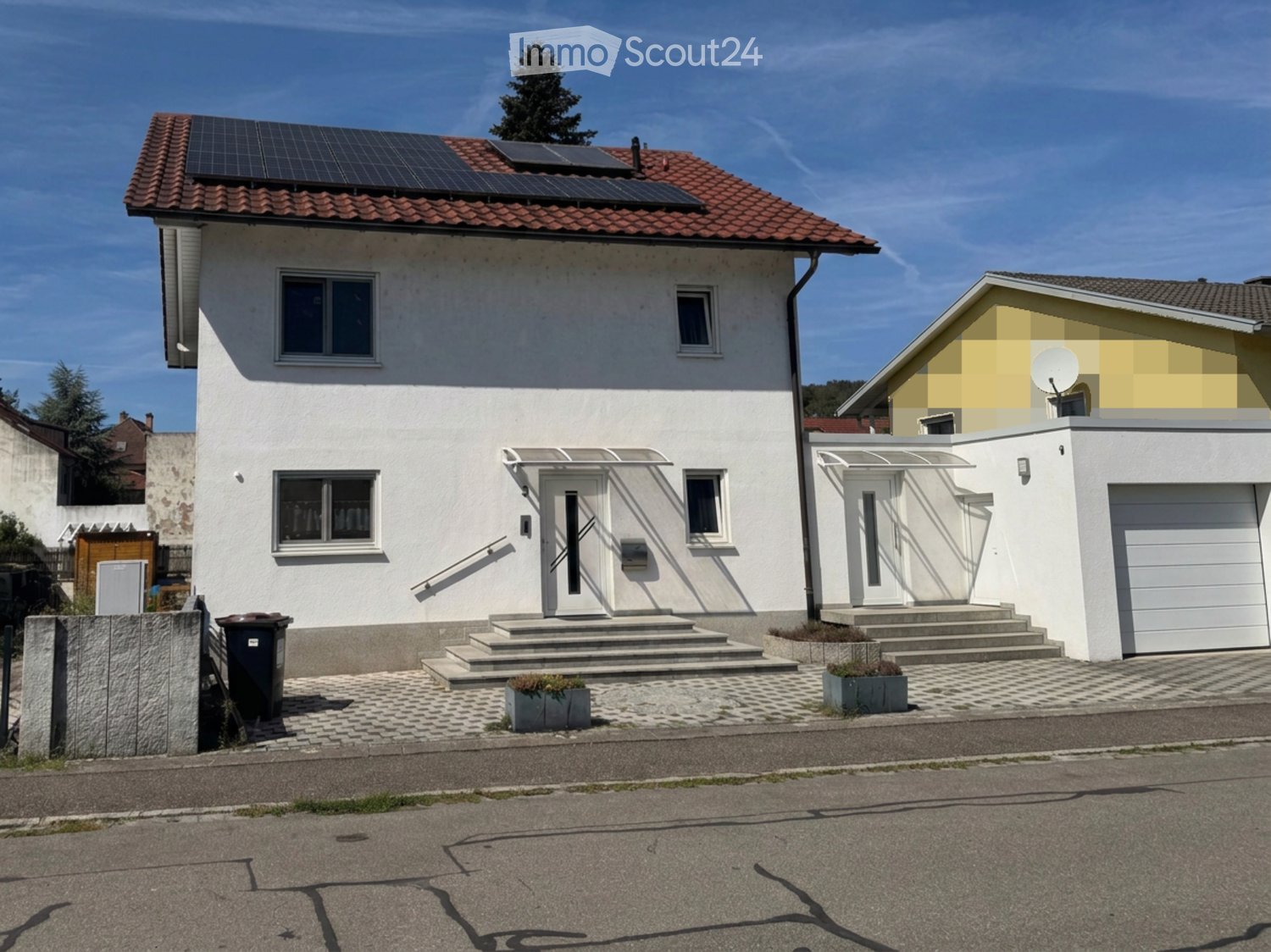 Two-story house with white exterior, red-tiled roof, solar panels, garage, and steps leading to the entrance.