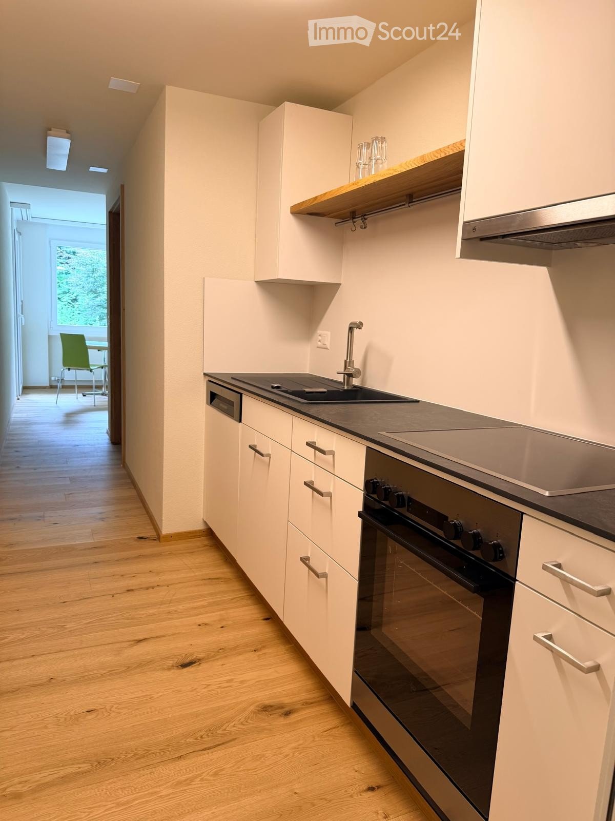 Modern kitchen with white cabinets, stainless steel appliances, and wooden flooring. Features an oven, sink, and faucet.