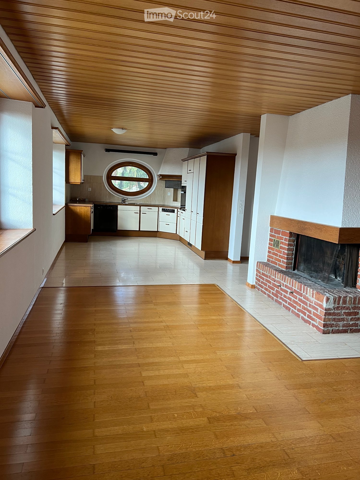 Open-plan living and dining area with wooden flooring, fireplace, and integrated kitchen featuring cabinets, a dishwasher, and a sink.