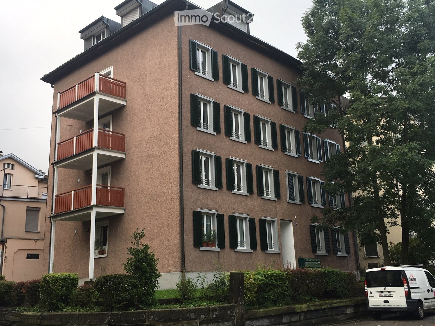 5-story building, red balconies, multiple windows, brown walls, entrance door, plant pots on balconies