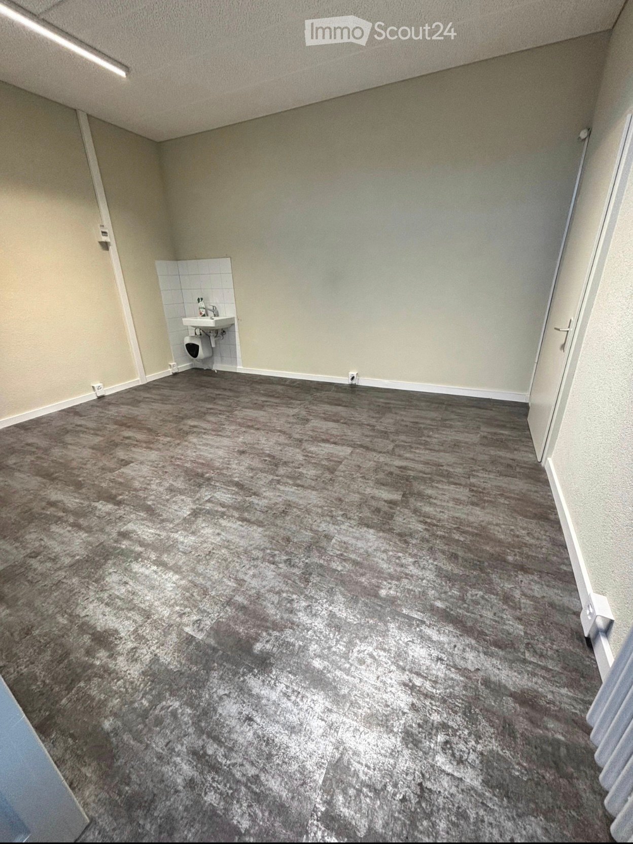 Empty room with grey tiled floor, white walls, and a small sink and toilet in the corner.