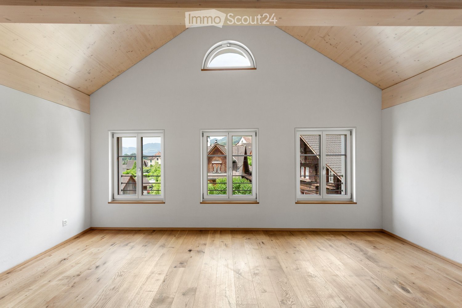 Empty room with wooden flooring, white walls, and multiple windows offering views of the outside. The ceiling features exposed wooden beams and a skylight.