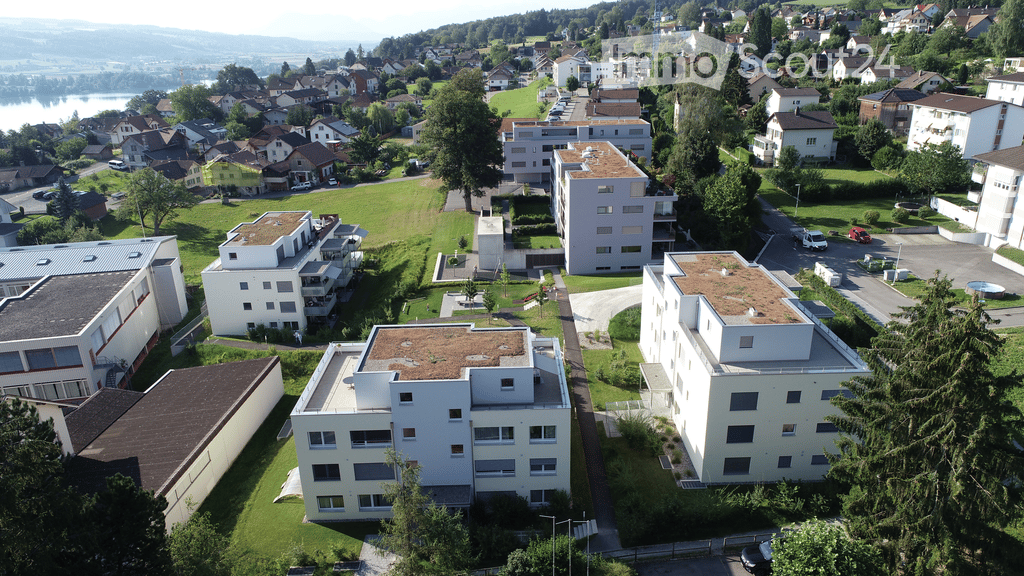 Aerial view of a residential area with multiple apartment buildings, green spaces, parking lots, and a swimming pool.