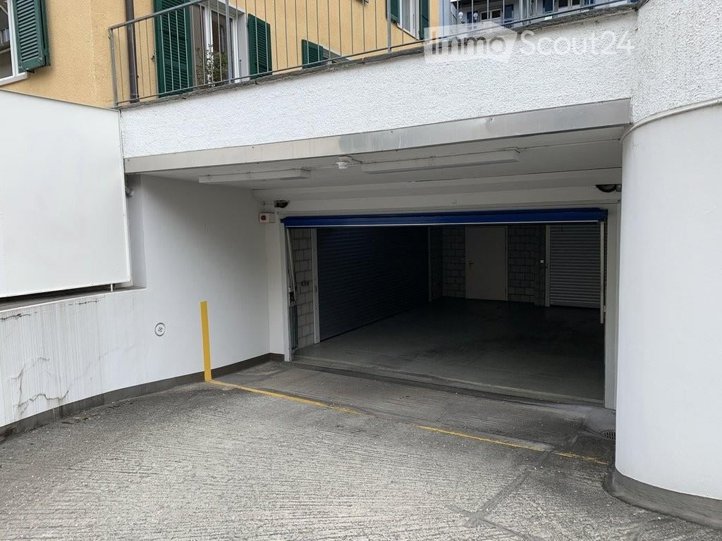 Underground garage with multiple parking spaces, white walls, and a blue overhead door.