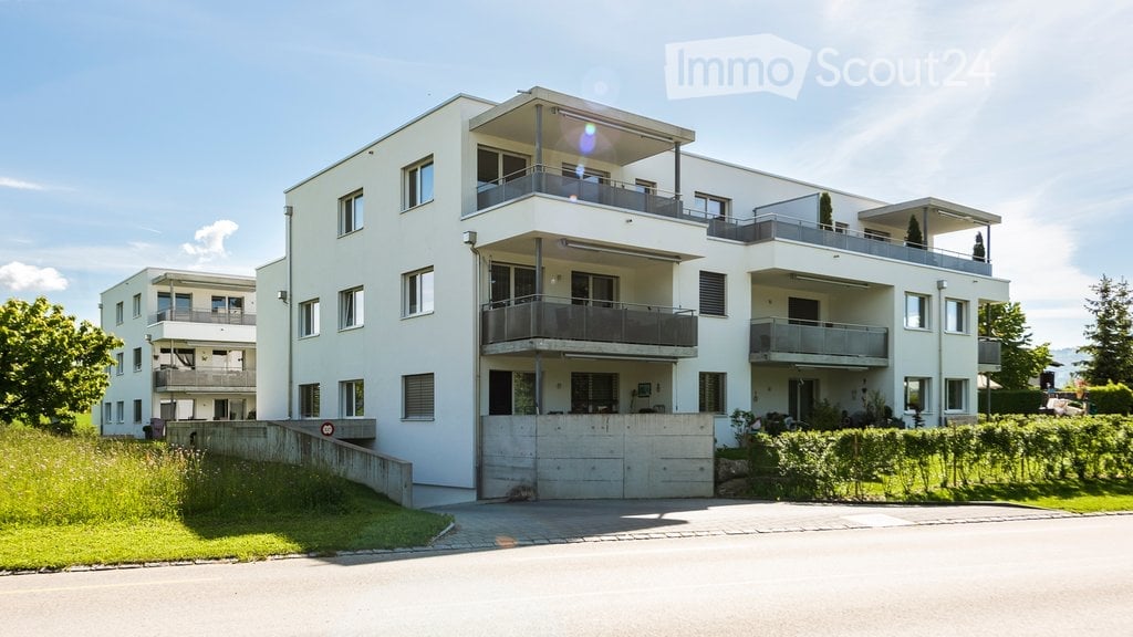 Modern multi-story residential building with white exterior, multiple balconies, and a garage entrance.
