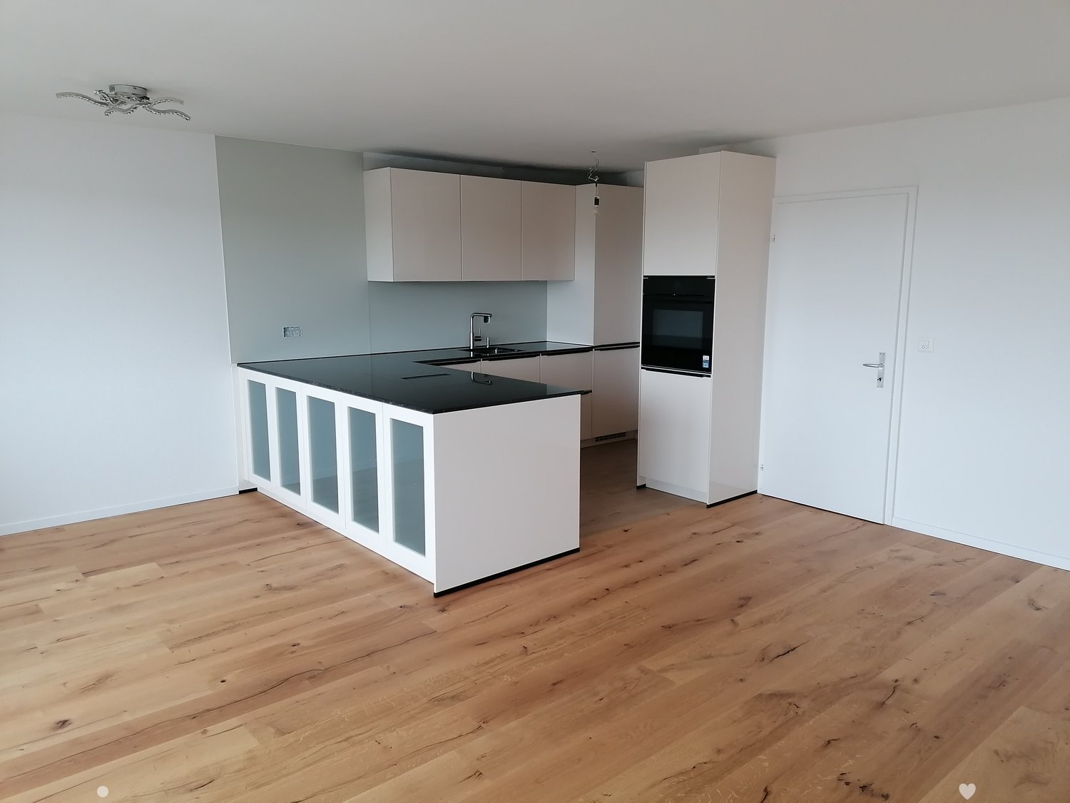 Modern kitchen with white cabinets, black countertop, and wooden flooring.