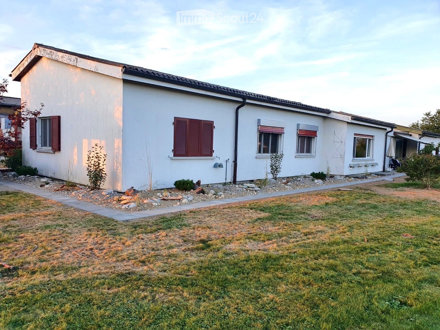 Single-story house with white walls, red shutters, and a well-maintained lawn.