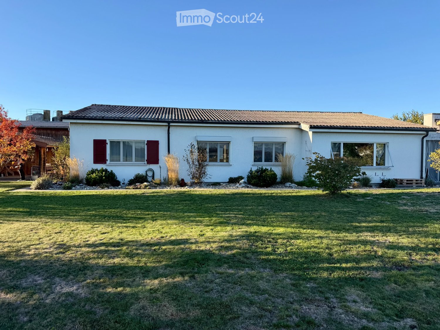 Single-story white house with a tiled roof, multiple windows, and a well-maintained lawn.