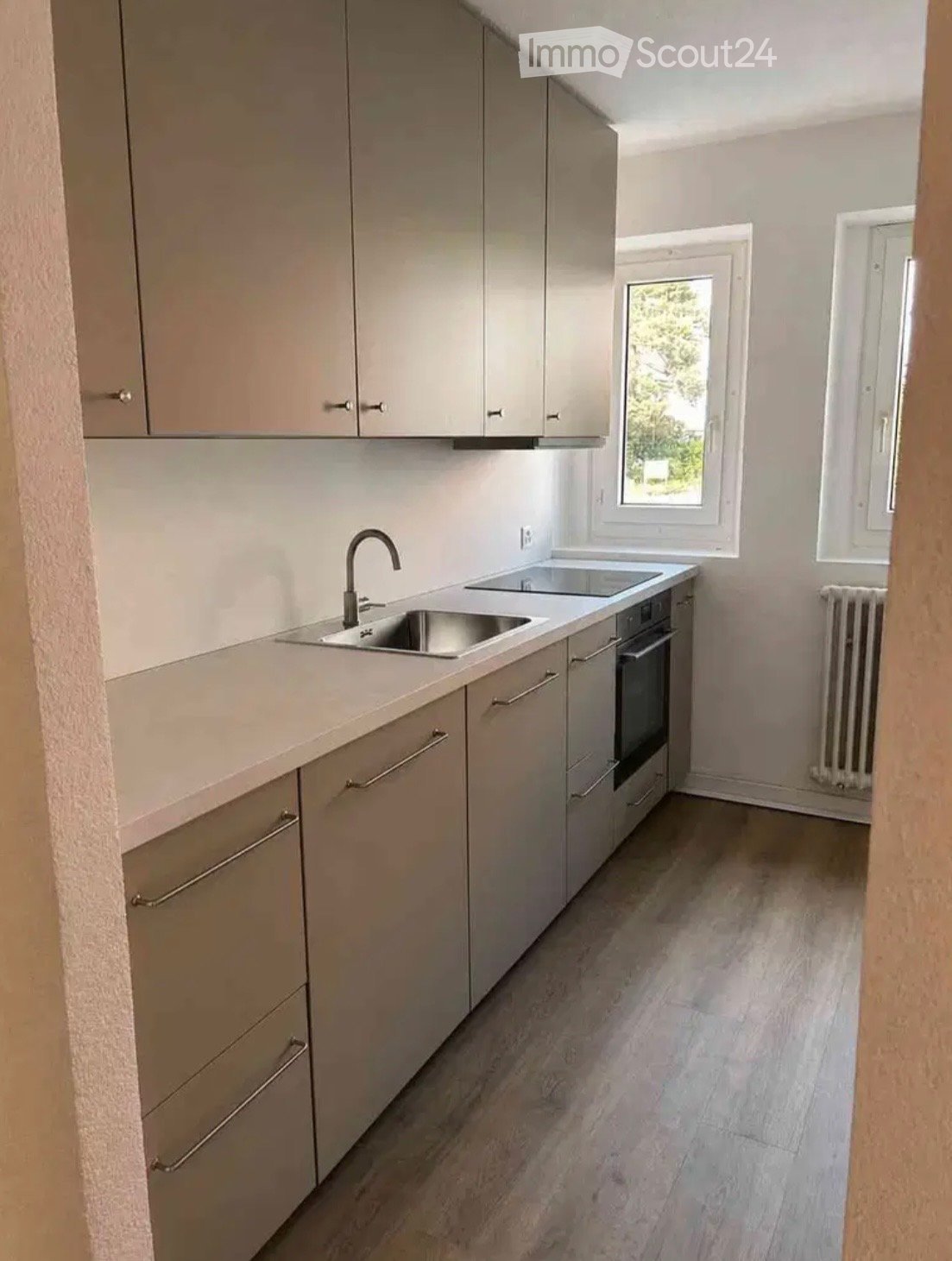 Modern kitchen with light grey cabinets, a double sink, and an oven. The space features light-colored countertops and a wooden floor.