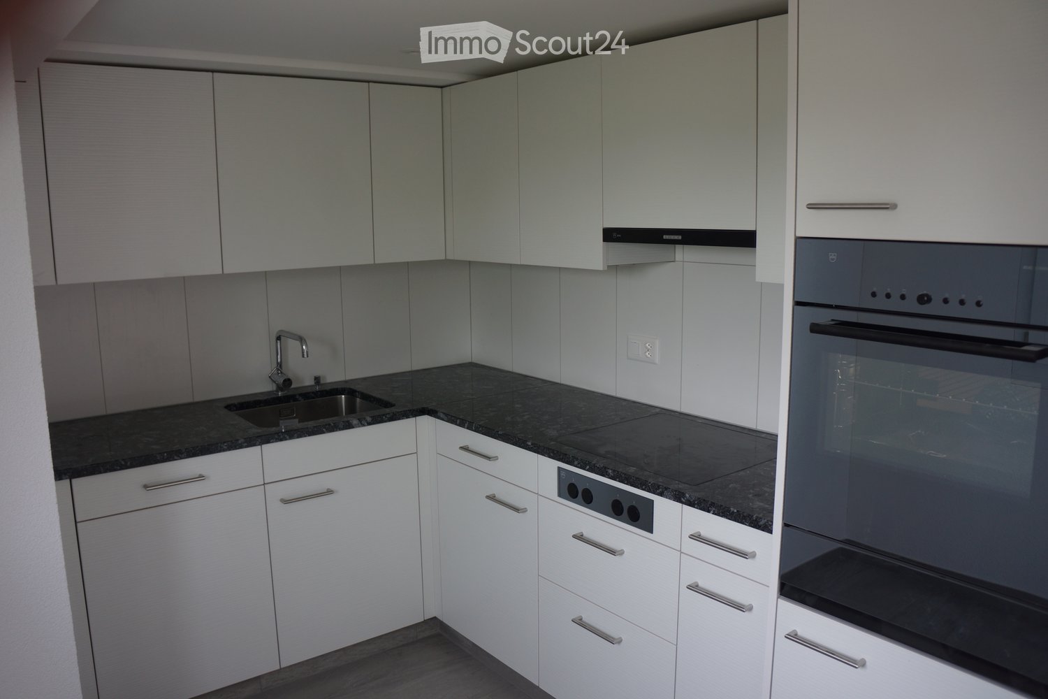 Modern kitchen with white cabinets, dark granite countertop, stainless steel sink and faucet, and built-in oven.