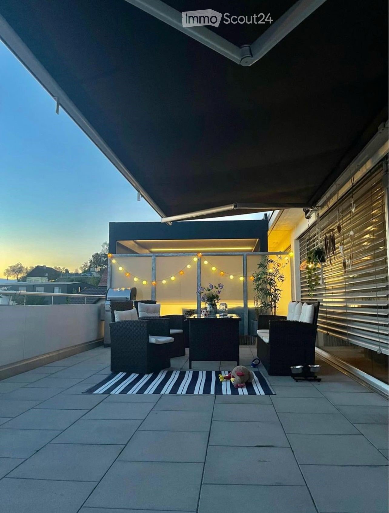 Modern rooftop terrace with a dining table, chairs, vase with flowers, rug, and a small toy on the floor.