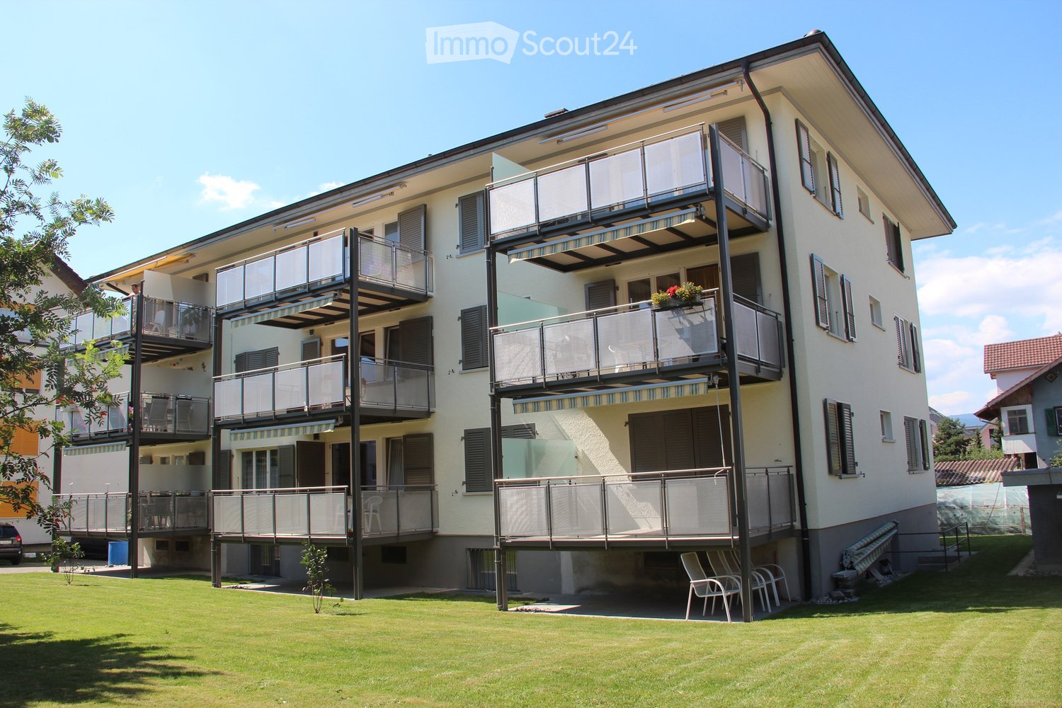 Modern multi-story residential building with balconies, white exterior, and green lawn in front.