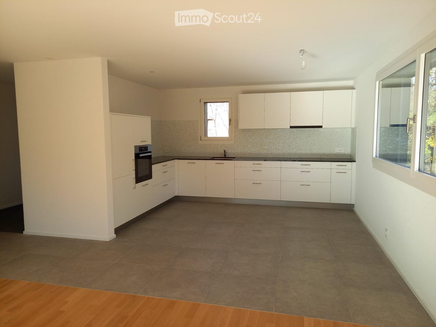 Empty kitchen with white cabinets, dark countertops, and tiled floor. Features include an oven, sink, and windows allowing natural light.