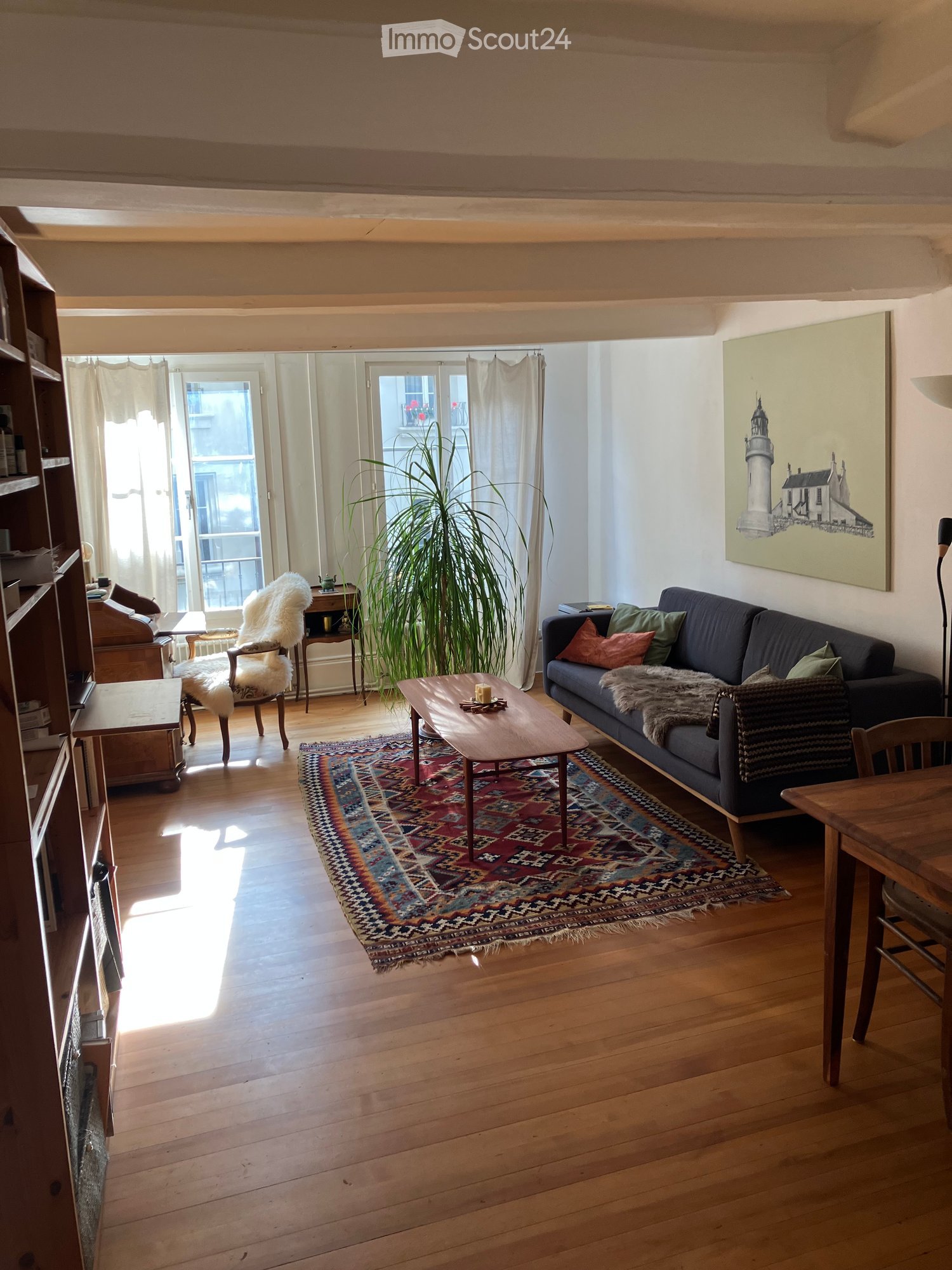 wooden floor, wooden bookcase, wooden chair, wooden table, couch, coffee table, rug, plant, large windows, painting on wall