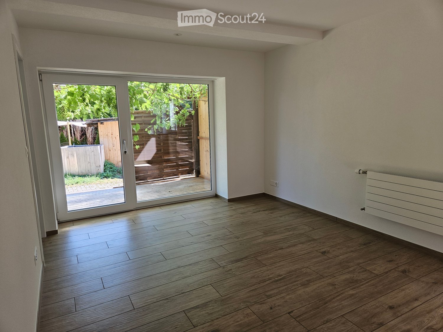 Empty room with wooden flooring, light-colored walls, and a sliding glass door leading to an outdoor deck.