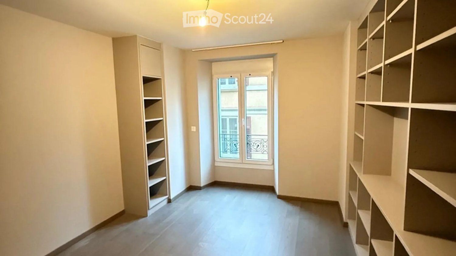Empty room with built-in shelving units on both sides, a large window with a view, and a door leading to a balcony.