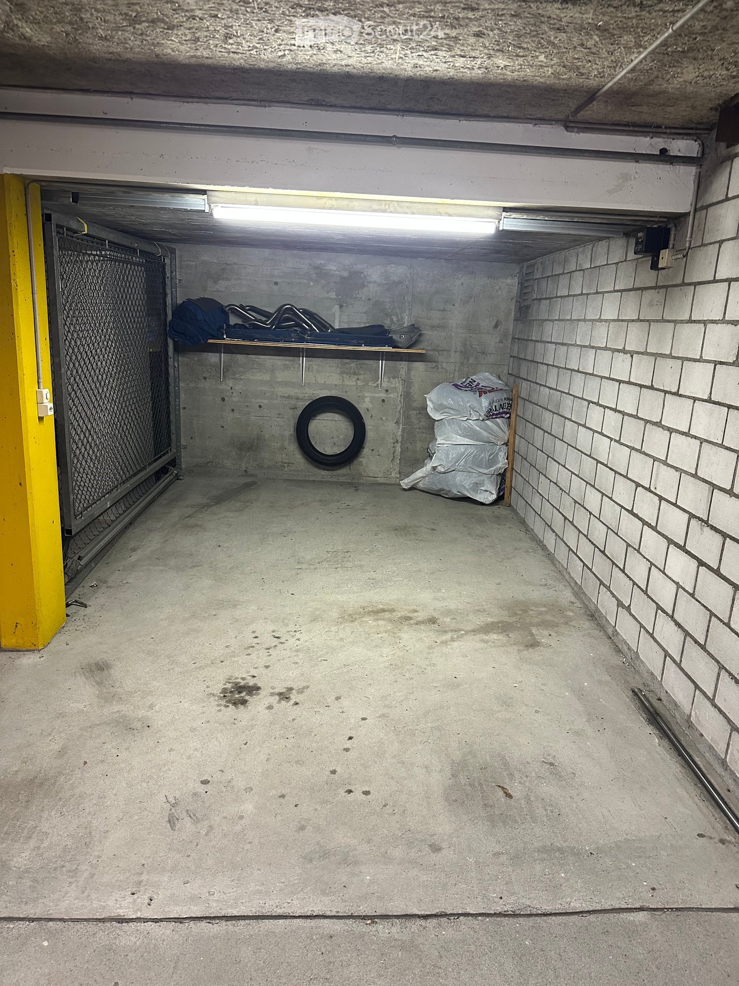{"visible_features": ["Garage"], "type": "Garage", "objects": [], "description": "Underground garage with concrete floor, brick wall, metal gate, and storage items including bags and a tire."}