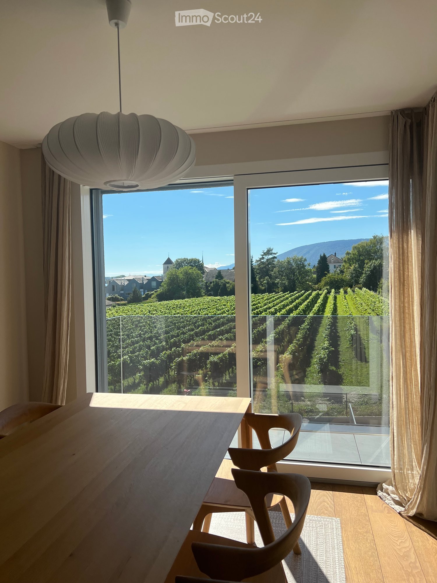 Bright dining area with large windows offering scenic views of vineyards and mountains, featuring a wooden dining table and chairs.
