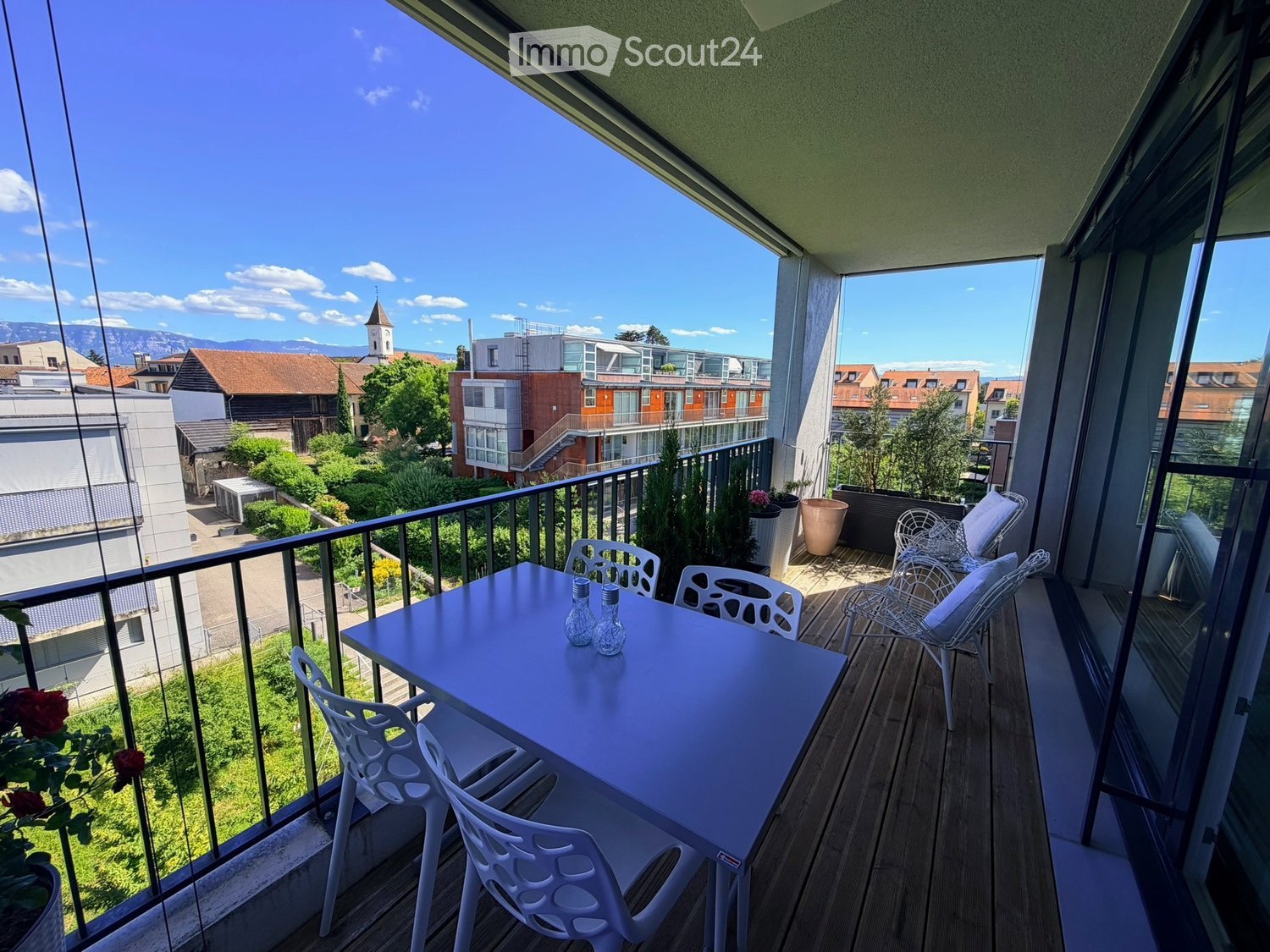 Balcony with wooden decking, white table and chairs, potted plants, and scenic city view.
