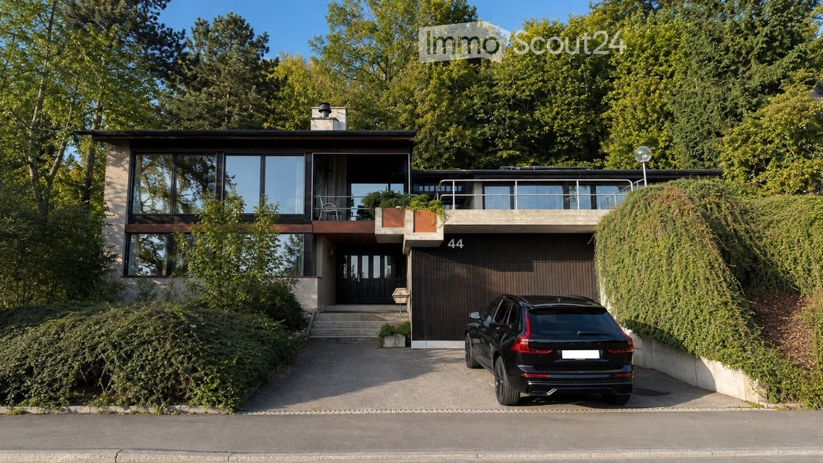 Modern two-story house with large windows, a garage, and a parked car in front.
