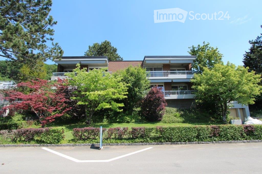 Two-story brick building with balconies, surrounded by lush greenery and trees.