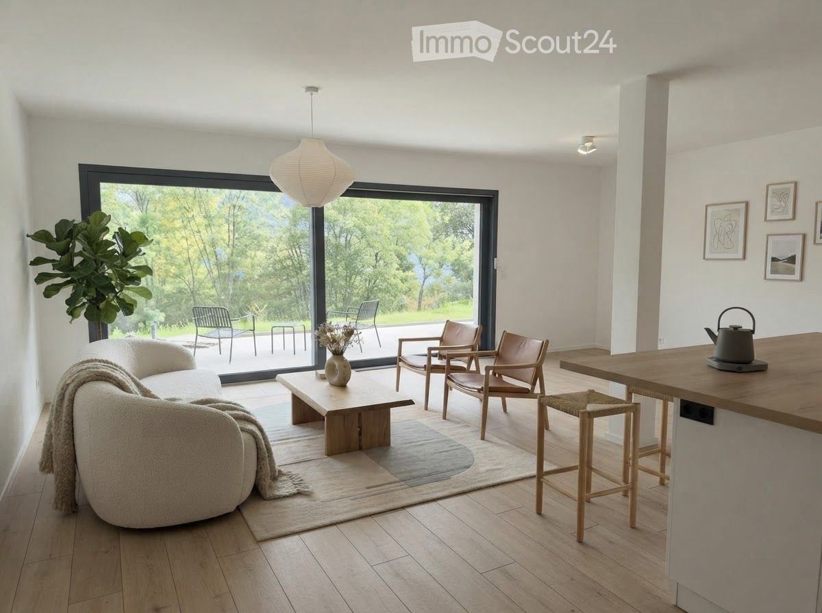 Bright living room with large windows offering a scenic view, featuring a white sofa, wooden coffee table, chairs, and a kitchen island with a teapot.
