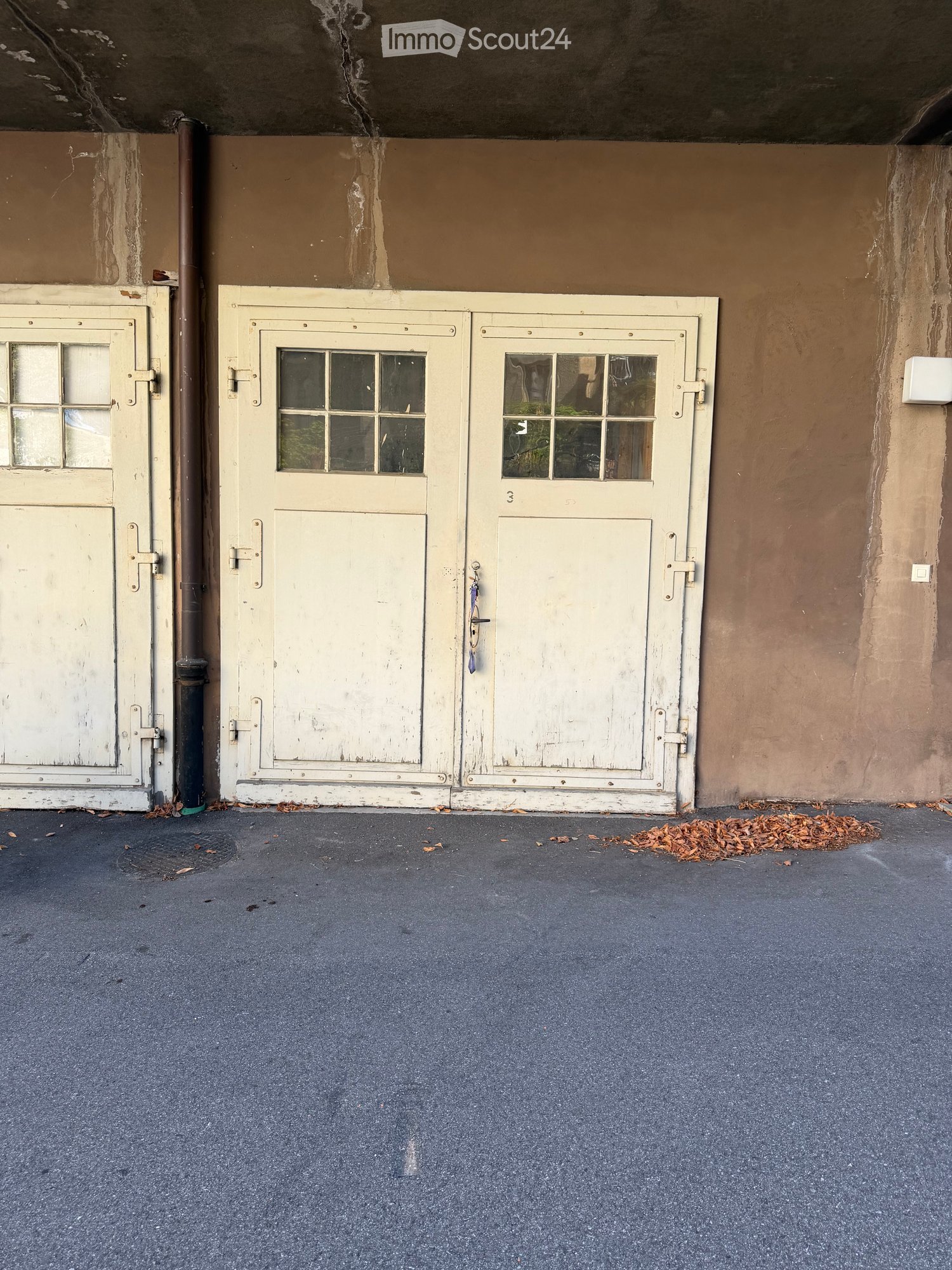 Empty garage with two large white doors, a dark grey floor, and a small pile of leaves near the right door.