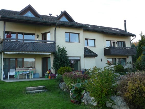 Two-story house with white walls, multiple windows, balconies, and a well-maintained garden.