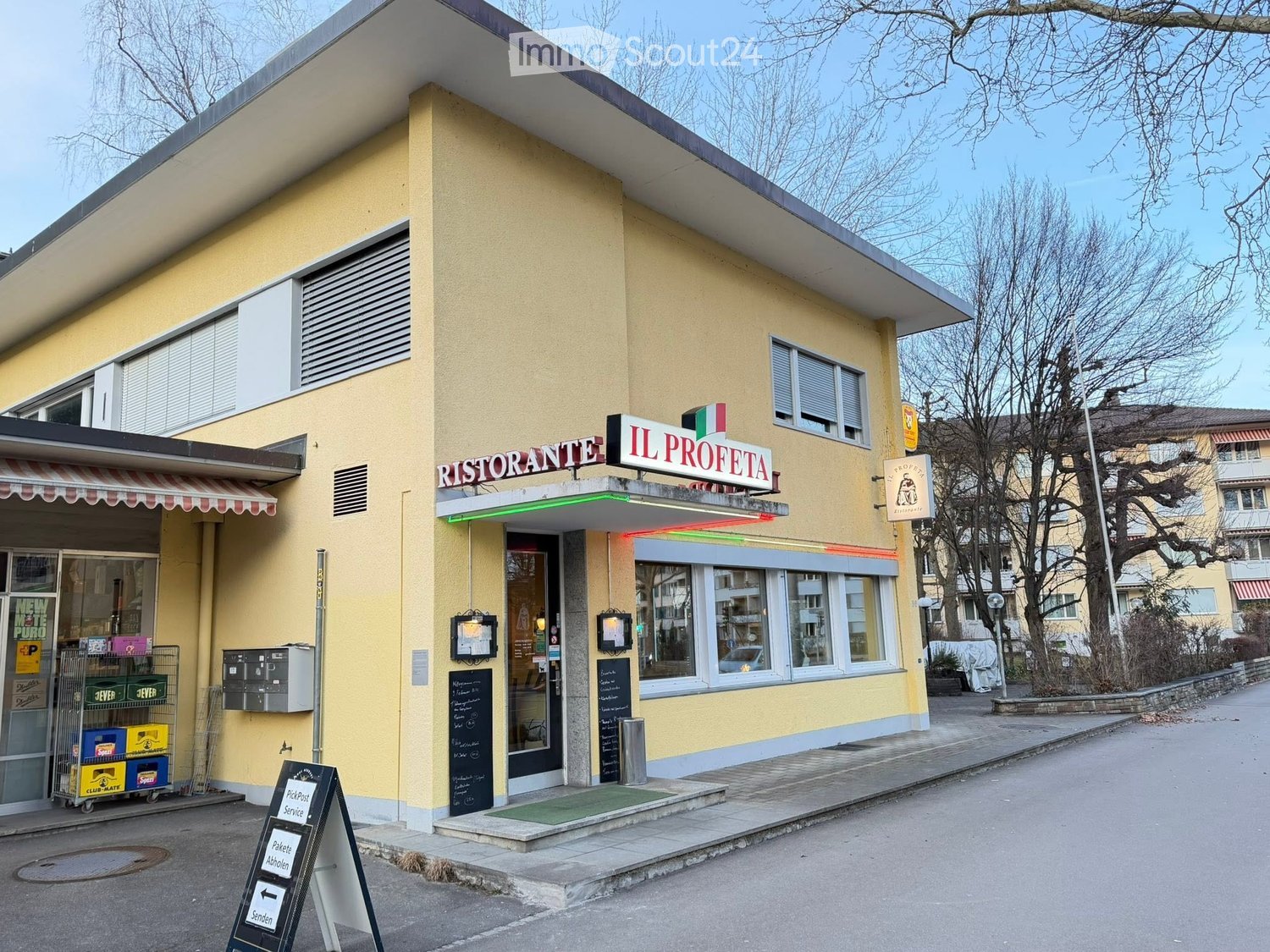 Two-story yellow building with a restaurant sign reading "IL PROFETA" and "RISTORANTE" above the entrance. Features a striped awning, glass windows, and a sidewalk with a small green doormat.