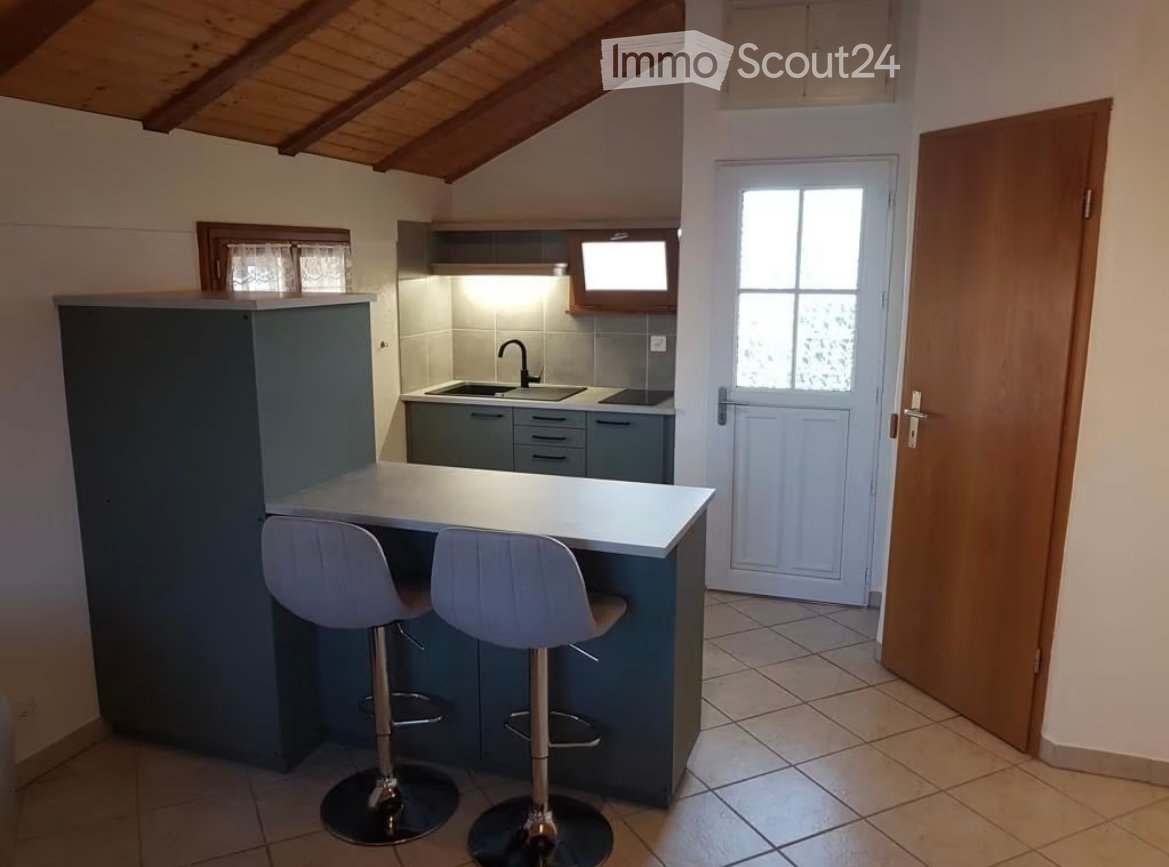 Modern kitchen with a grey cabinet island, two white stools, a sink with a faucet, and built-in cabinets.