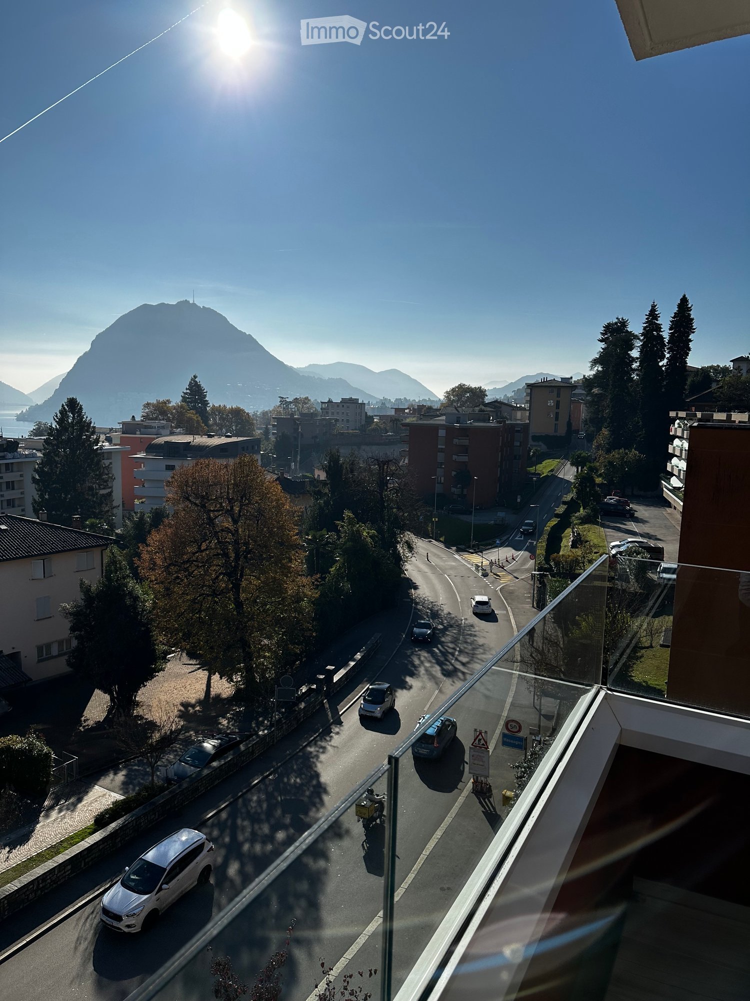Balcony overlooking a road with cars, trees, and distant mountains and lake.