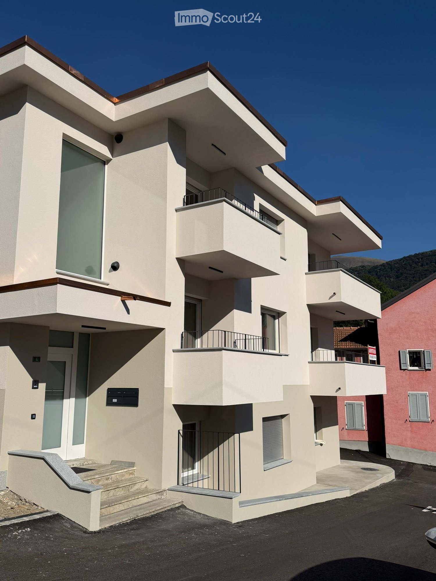 Modern two-story house with beige facade, large windows, balconies, and a staircase leading to the entrance.