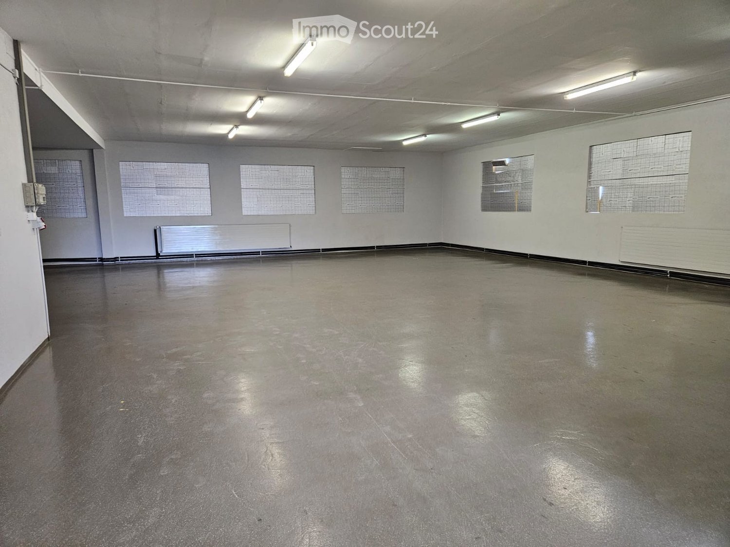 Empty room with bare walls, concrete floor, and large windows with metal grilles. No furniture or equipment present.