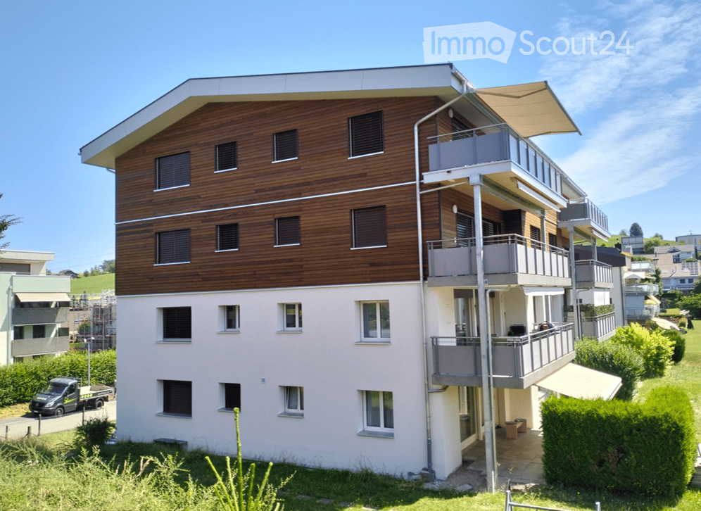 Modern two-story residential building with a combination of wooden and light-colored facades, multiple balconies, and contemporary design.