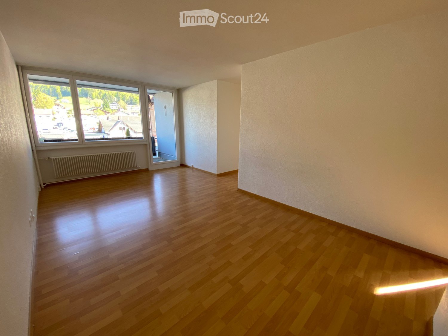 Empty room with wooden flooring, large windows, and a radiator on one wall. No furniture or equipment present.